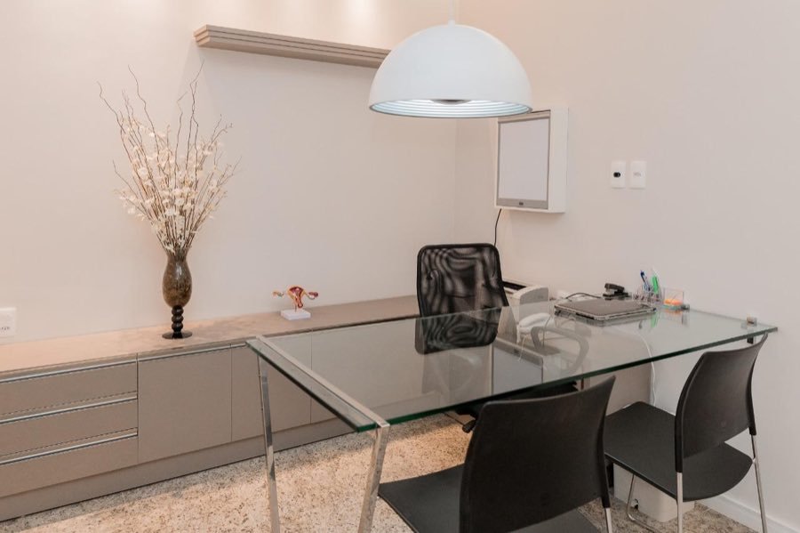 Consultório claro, com mesa de vidro e arranjo de flores