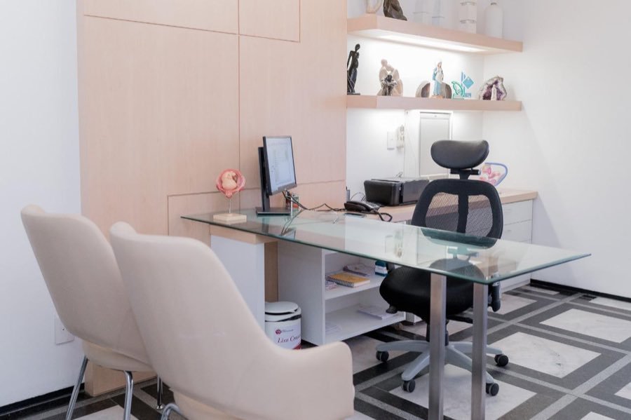 Consultório com mesa de vidro e duas poltronas para o acompanhante